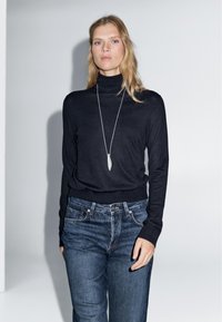 Black turtleneck sweater made of fine knit material, paired with denim jeans. Long sleeves and fitted design accentuate the silhouette.