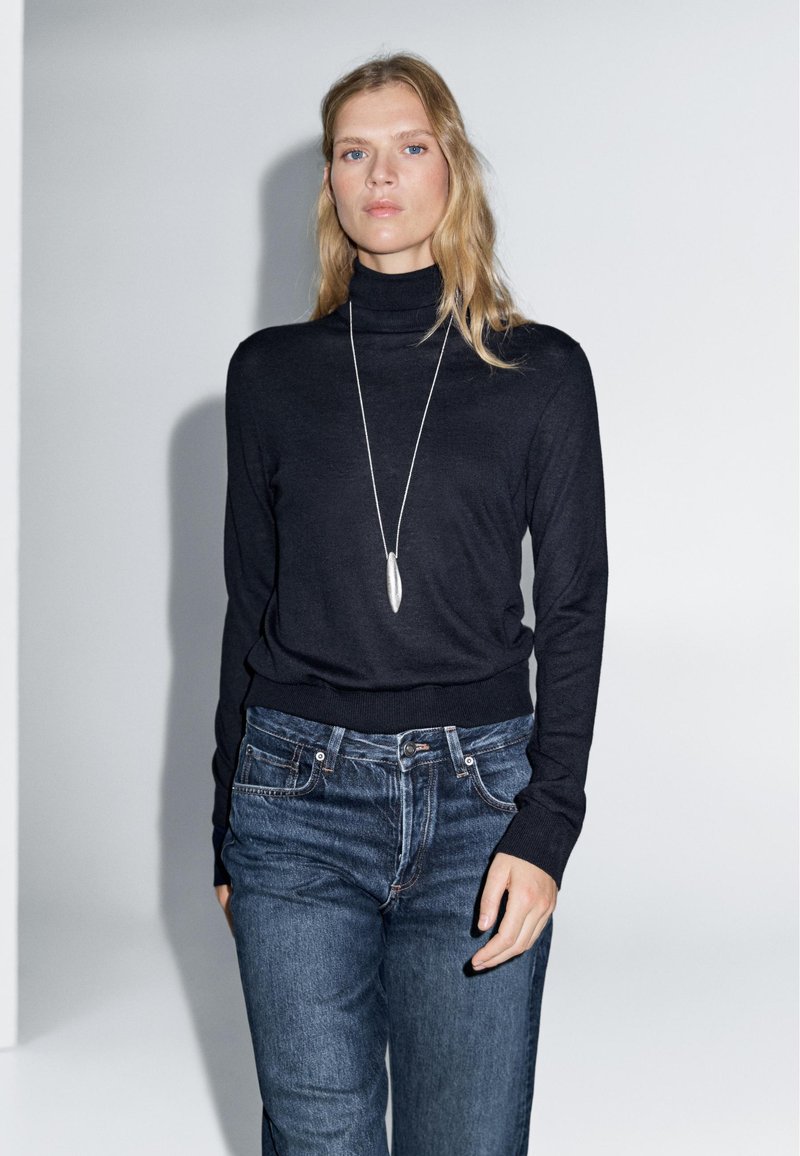 Black turtleneck sweater made of fine knit material, paired with denim jeans. Long sleeves and fitted design accentuate the silhouette.