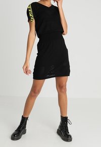 Robe tricotée noire avec un col en V et un top court. Présente un motif texturé et une taille ajustée, assortie de bottes de combat noires à lacets.