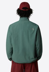 Leichte grüne Jacke mit Stehkragen, elastischen Bündchen und verstellbarem Saum. Verfügt über ein kleines gesticktes Logo auf dem Rücken.