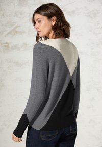 Grauer, gerippter Pullover mit einem geometrischen Design, das aus hellgrauen, dunkelgrauen und schwarzen Abschnitten besteht. Weicher Stoff, Rundhalsausschnitt und lange Ärmel.