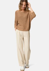 Maglione di maglia marrone con una vestibilità comoda, abbinato a pantaloni larghi beige chiaro e sneakers bianche, creando un look casual.