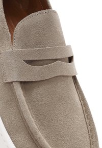 Beige suede loafers feature a cut-out strap design, textured surface, and contrasting white sole, showcasing clean lines and minimal detail.
