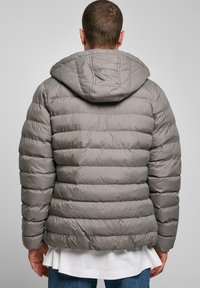 Grå pufferjakke med hætte. Har et quiltet design med vandret syning. Glat, blankt stof med en let glans.