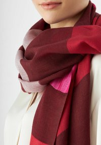 Bordeaux en roze sjaal met een patroon, gemaakt van zachte stof, met een mix van texturen en kleuren, die om de nek is gedrapeerd.