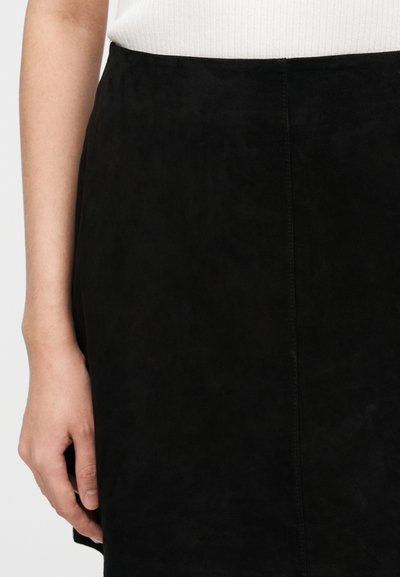 Black suede skirt with a smooth texture and structured design, featuring a side seam and close-fitting silhouette. Hand resting on the garment.