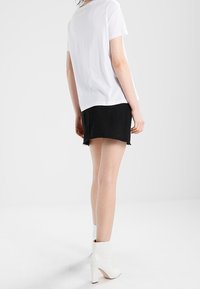 Camiseta blanca de manga corta, pantalones cortos de denim negro con dobladillo deshilachado y botas blancas hasta el tobillo con tacones altos. Vista trasera contra un fondo claro.