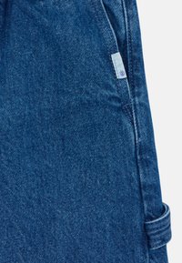 Modra jeansa tkanina ima rahlo teksturo z majhno tkanim oznako, na kateri je prikazan logotip. Material je trpežen z klasičnim ravnim krojem.