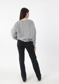 Maglione grigio lavorato a maglia con motivo strutturato, vestibilità ampia e spalle scese, abbinato a pantaloni neri aderenti, visto da dietro.