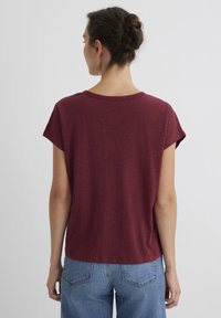 Burgundy short-sleeve t-shirt with a crew neck, relaxed fit, soft texture, and a slightly rounded hem; worn with light blue jeans.