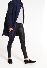 Námořnický vlněný kabát, šedý svetr, černé kožené kalhoty a černé semišové slip-on boty s metalickými špičkami. Přizpůsobený střih a elegantní design.