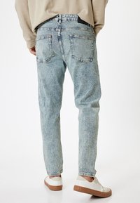 Jeans de mezclilla de tiro alto en azul claro con una textura desteñida. Presentan dos bolsillos traseros y un diseño de pierna recta. Se usan con zapatillas blancas.
