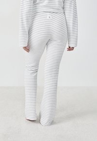 Pantalons de lounge rayés gris et blanc en tissu doux, présentant une coupe décontractée et des jambes évasées, vus de derrière.