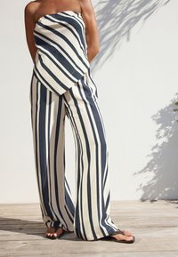 Striped, wide-leg pants in navy and cream cotton fabric, featuring a draped, strapless top section with diagonal lines and a lightweight texture.