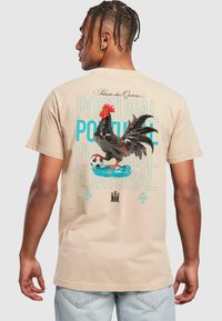 Bežinis medvilninis marškinėlis su juodu gaidžiu iliustracija, raudonu šukuosena, futbolo kamuoliu ir mėlynomis akcentais. Žodis: "Portugalija" išryškintu šriftu.