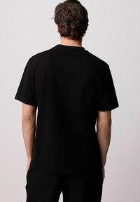 Zwarte katoenen t-shirt met korte mouwen en ronde halslijn, met een gladde textuur en rechte zoom, gezien vanaf de achterkant.