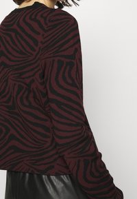 Burgundská svetr s černým proužkovaným vzorem zebra. Má dlouhé rukávy a kulatý výstřih, vyrobený z měkké, texturované tkaniny.