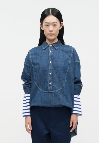 Τζιν πουκάμισο με γιακά, κλείσιμο με κουμπιά στο μπροστινό μέρος και μεγάλο τσέπη. Διαθέτει ριγέ μανίκια σε μπλε και λευκό.