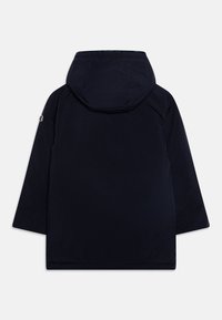 Chaqueta azul marino con capucha, que presenta un tejido suave y mate, mangas largas y un logo sutil en el hombro izquierdo.