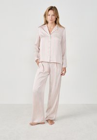 Pijamas a rayas en rosa claro y blanco, que incluyen una camiseta de botones con un bolsillo y pantalones de corte holgado, hechos de una tela suave.