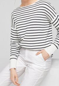 Maglione a righe in bianco e blu navy, con scollo ampio e polsini a coste. Abbinato a pantaloni bianchi, evidenziando un look casual.