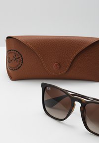 Ruskean tekstuurihohto, jossa on napsautussuljin. Mustat kilpikonnakuoriset aurinkolasit, joissa on liukuväri ruskeat linssit. Ray-Ban-logo linsseissä ja kotelossa.