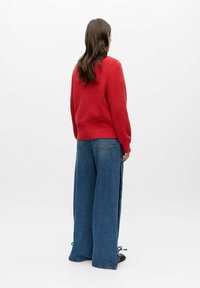 Suéter rojo de punto con textura acanalada. Combinado con pantalones vaqueros de mezclilla azul de pierna ancha. El suéter tiene un cuello redondo y mangas largas.