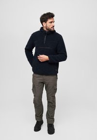 Pull en polaire navy avec demi-zippé, surface texturée, design dédoublé et poche zippée. Associé à un pantalon cargo olive et des bottes noires.