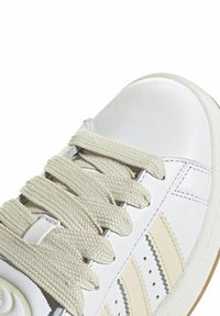 White leather sneaker with beige accents, textured laces, and rubber sole. Features three narrow beige stripes and stitched details.