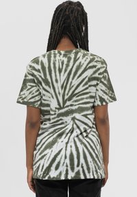 Short-sleeve t-shirt made of cotton, featuring a green and white tie-dye pattern with a spiraling design. The fabric has a soft texture.