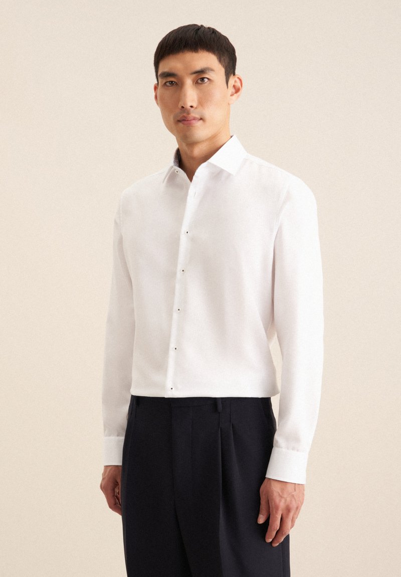 Witte button-up shirt met een gladde textuur, voorzien van een standaardkraag en subtiele knoopaccenten. Draag het met donkere, op maat gemaakte slacks.