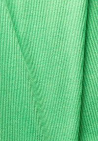 Tissu côtelé vert clair avec de fines lignes verticales et de subtils plis créant des ombres douces et une texture.