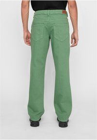 Žalios medvilnės kelnes su tiesiais kojų kirpimais, užpakalinėmis kišenėmis ir rudos odos lopu ties liemeniu.