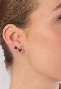 Schwarze Steckerohrringe mit einem kreisförmigen und einem V-förmigen Design, aus Metall mit matter Oberfläche, präsentiert am Ohr eines Modells.