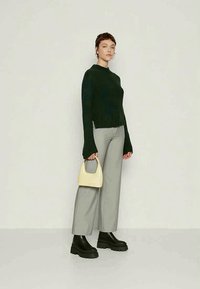 Knit dark green sweater, gray wide-leg pants, black chunky boots, and a small yellow bag. Sweater has long, flared sleeves and a round neck.