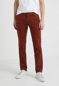 Pantaloni chinos rossi in cotone con una vestibilità slim, chiusura con bottone e design a cinque tasche. Abbinati a sneakers bianche, che evidenziano uno stile casual.