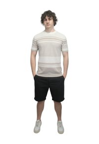 Camicia a maniche corte a righe beige chiaro abbinata a pantaloni corti neri. Il modello sta in piedi con le mani in tasca, indossando sneakers bianche.