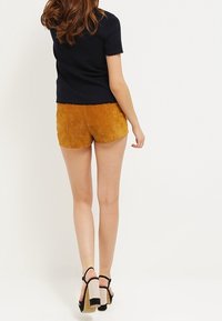 Pantaloni corti in suede arancione bruciato, con una finitura texturizzata. Abbinati a una maglietta nera a maniche corte e sandali con tacco a blocco neri e marroni.