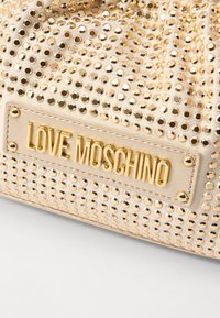 Gouden handtas versierd met pailletten, met een gestructureerde beige stoffen basis, voorzien van een metalen logo plaat "LOVE MOSCHINO" en een ronde vorm.