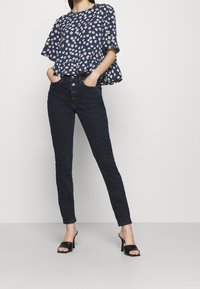 Navy floral blouse with short sleeves, fitted black jeans with a high waist, and black heeled mules, creating a casual outfit.