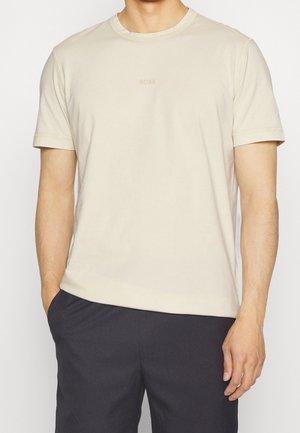 Beige Baumwoll-T-Shirt mit Rundhalsausschnitt, kurzen Ärmeln und einem dezenten "BOSS"-Logo auf der Brust, kombiniert mit dunklen Shorts.