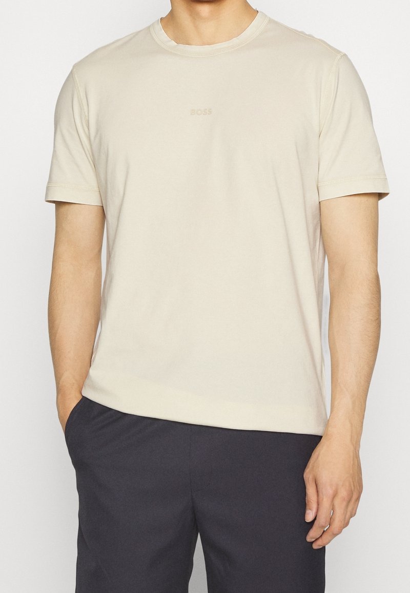 T-shirt en coton beige avec un col rond, des manches courtes et un logo « BOSS » subtil imprimé sur la poitrine, associé à un short sombre.