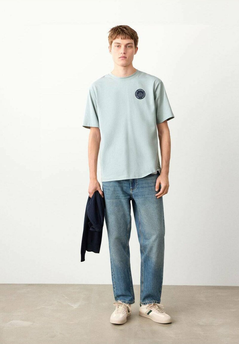 Tricou din bumbac albastru deschis, cu decolteu rotund, mâneci scurte și un detaliu logo în zona pieptului. Asortat cu blugi din denim cu spălare medie.