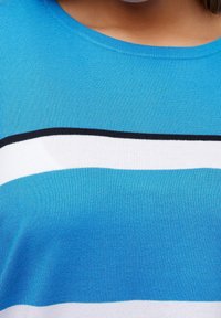 Krátký rukáv, tričko s kulatým výstřihem, které má vodorovné pruhy v odstínech modré, bílé a černé; vyrobeno z žebrované tkaniny s texturovaným povrchem.