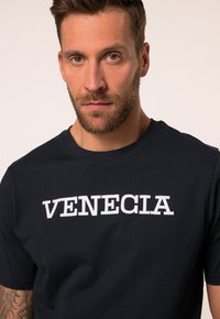 Camiseta de algodón azul marino de mangas cortas con bordado blanco de la inscripción "VENECIA" en el pecho. Textura suave, diseño casual.