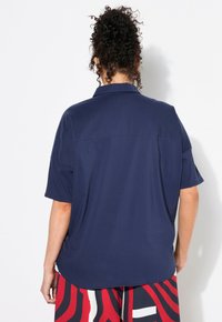 Camicia a maniche corte blu navy con colletto classico, caratterizzata da una texture liscia e una vestibilità comoda. Sul retro presenta un semplice design a yoke.