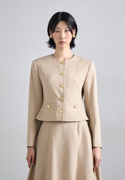 Beige Jacke mit taillierter Silhouette, rundem Halsauschnitt und goldenen, rosenförmigen Knöpfen, kombiniert mit einem passenden Rock. Glatte Stoffstruktur.