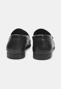 Schwarze Leder-slipper mit glatter Textur, rundem Rücken und minimalen Nähdetails. Flache Sohlen und keine sichtbaren Hardware-Elemente.
