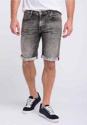 Pantalones cortos de mezclilla gris con un acabado ligeramente desgastado, puños enrollados y diseño de cinco bolsillos. Combinados con zapatillas de ante azul marino y cordones blancos.