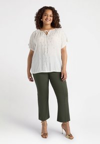 Bílá lehká blůza se zlatými akcenty, kulatým výstřihem se zavazováním, krátkými rukávy, spárovaná s olivově zelenými úzkými kalhotami a zlatými podpatky.